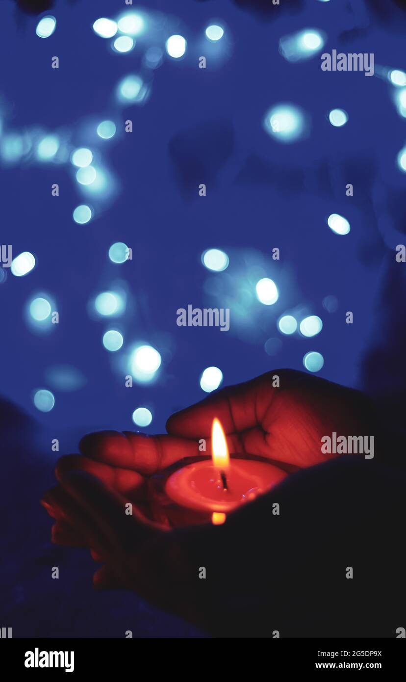 Candela bruciante nelle mani di una ragazza con luce bokeh. Candele di Natale. La luce a lume di candela si illumina nelle mani della donna. Concetto di preghiera, fede, religione. Foto Stock