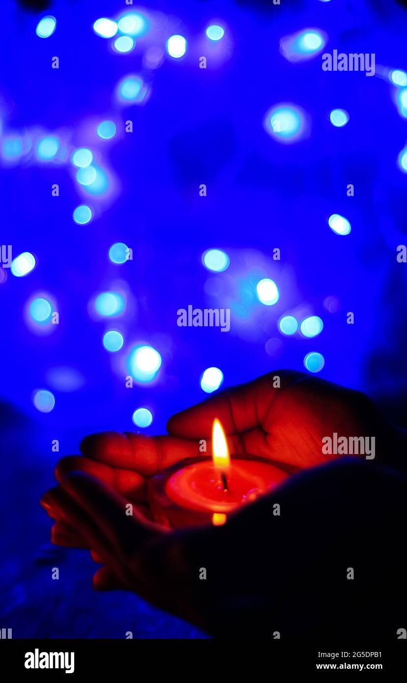 Candela bruciante nelle mani di una ragazza con luce bokeh. Candele di Natale. La luce a lume di candela si illumina nelle mani della donna. Concetto di preghiera, fede, religione. Foto Stock