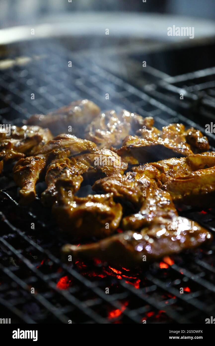 Zampe di pollo speziate e ali marinate con salsa di peperoncino grigliate su un fuoco fumante in un barbecue portatile Foto Stock