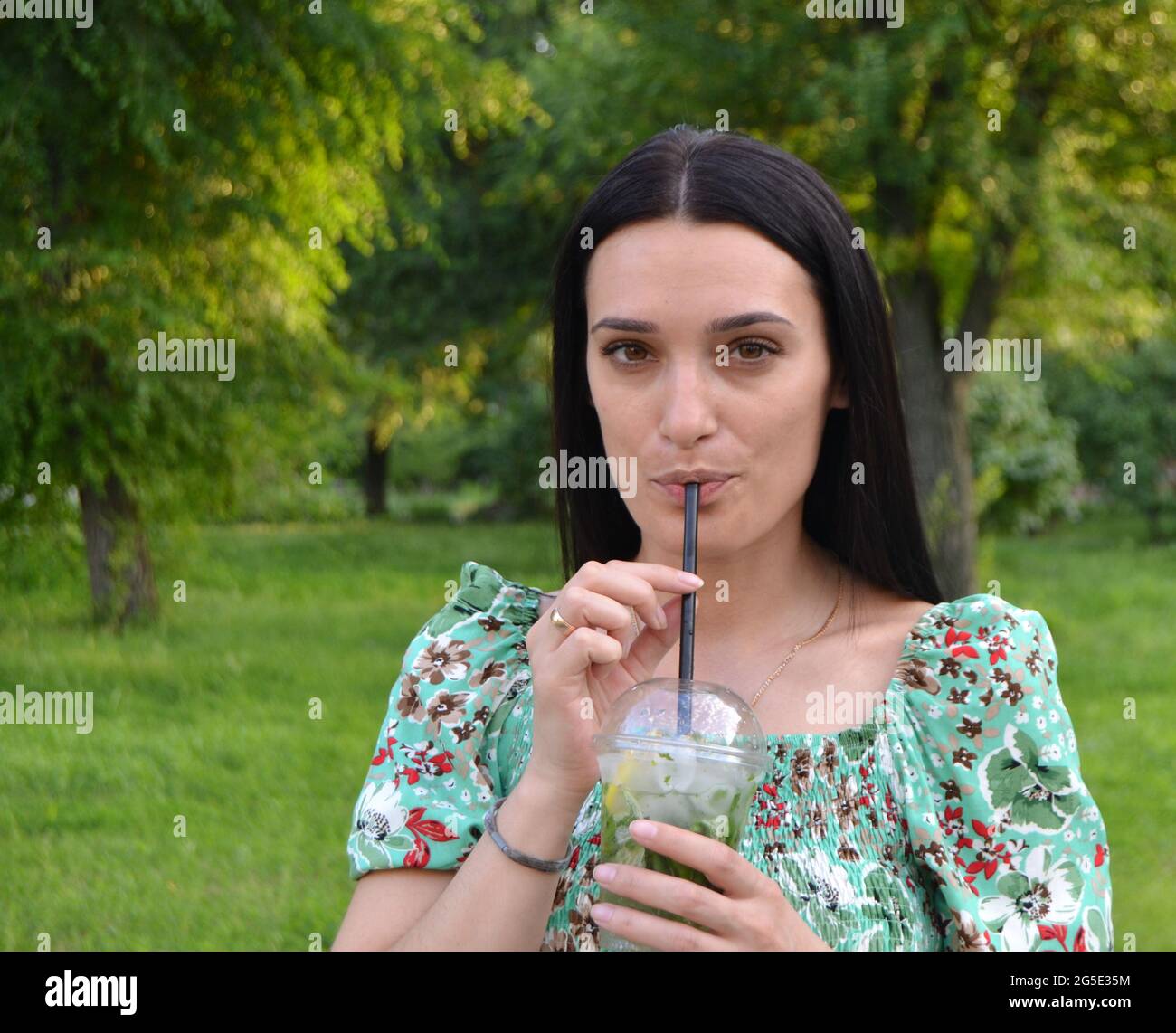 Donna beve felicemente mojito nel parco in estate. Foto Stock