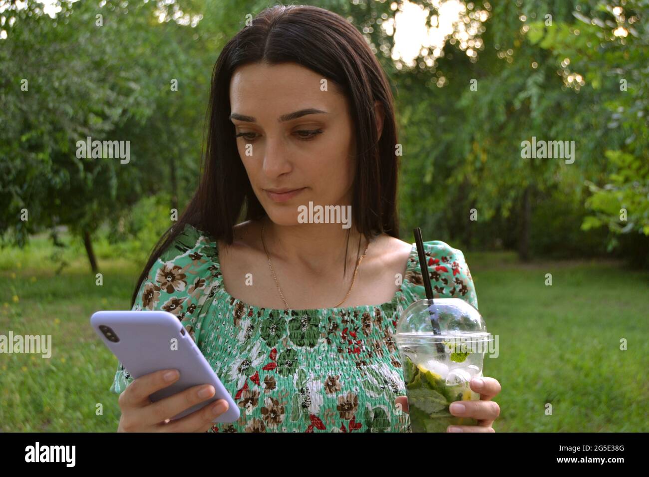 Donna beve mojito nel parco in estate e guardando il suo smartphone Foto Stock