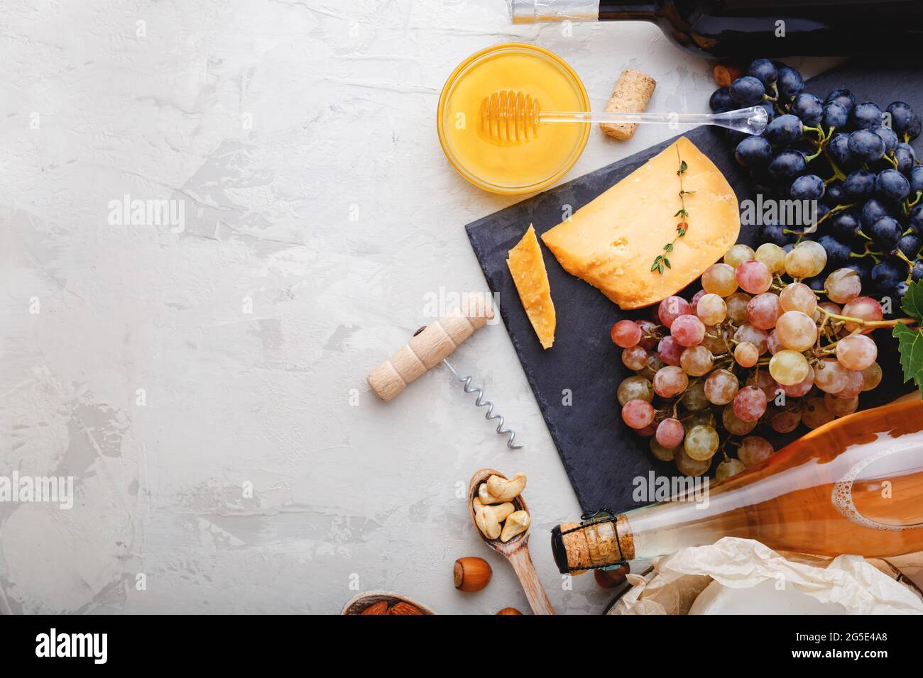 Cena romantica con spuntino a base di vino. Champagne rosato vino rosso in bottiglie con antipasto di varietà su tavola in cemento rustico grigio. Tagliere di formaggio Foto Stock