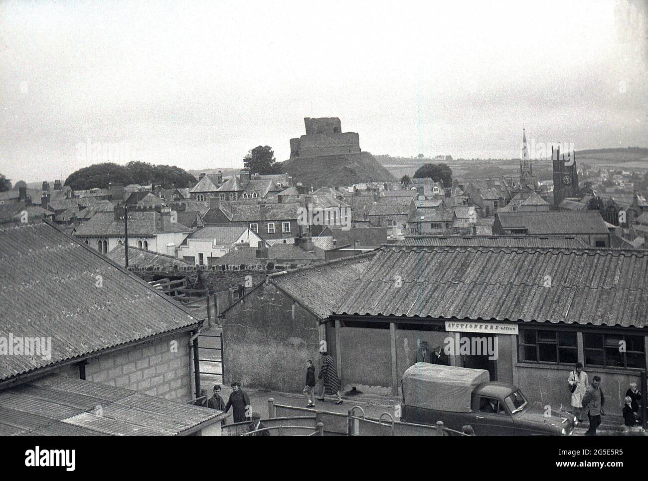 Anni '60, immagine storica che mostra una vista aerea sul mercato del bestiame di Launceston, Launceston, Cornovaglia, Inghilterra, Regno Unito con l'ufficio delle aste in primo piano e l'antico mastio e la torre del castello di Launceston sullo sfondo. La guglia della chiesa della Maddalena di S. Maria è visibile sul retro a destra. Foto Stock