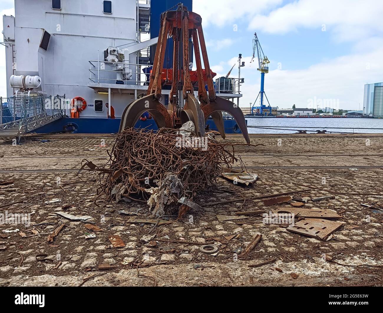rottami di manipolatore di gru con rottami di metallo sulla banchina sullo sfondo di una nave da carico a secco. Operazioni di carico e scarico di rottami metallici e s Foto Stock