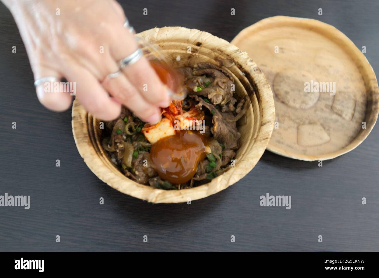 Mano della donna con Gyudon giapponese con uovo o recipiente di manzo giapponese con uovo in una ciotola di foglia di banan organico Foto Stock