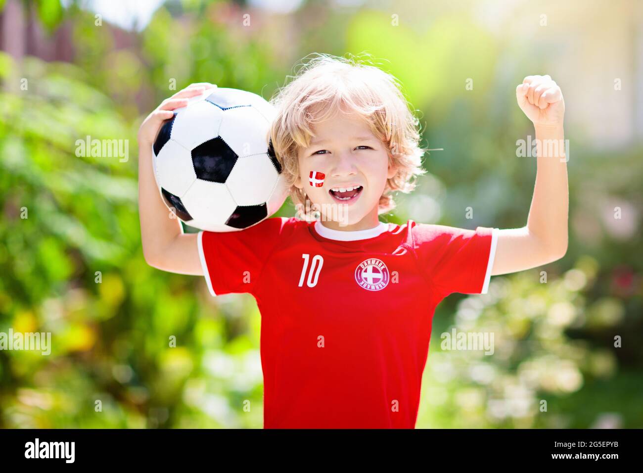Tifosi di calcio della Danimarca. I bambini danesi giocano a calcio e  festeggiano la vittoria sul campo all'aperto. Il sostenitore del team  Danmark. Piccolo ragazzo in maglia Dansk bandiera Foto stock -