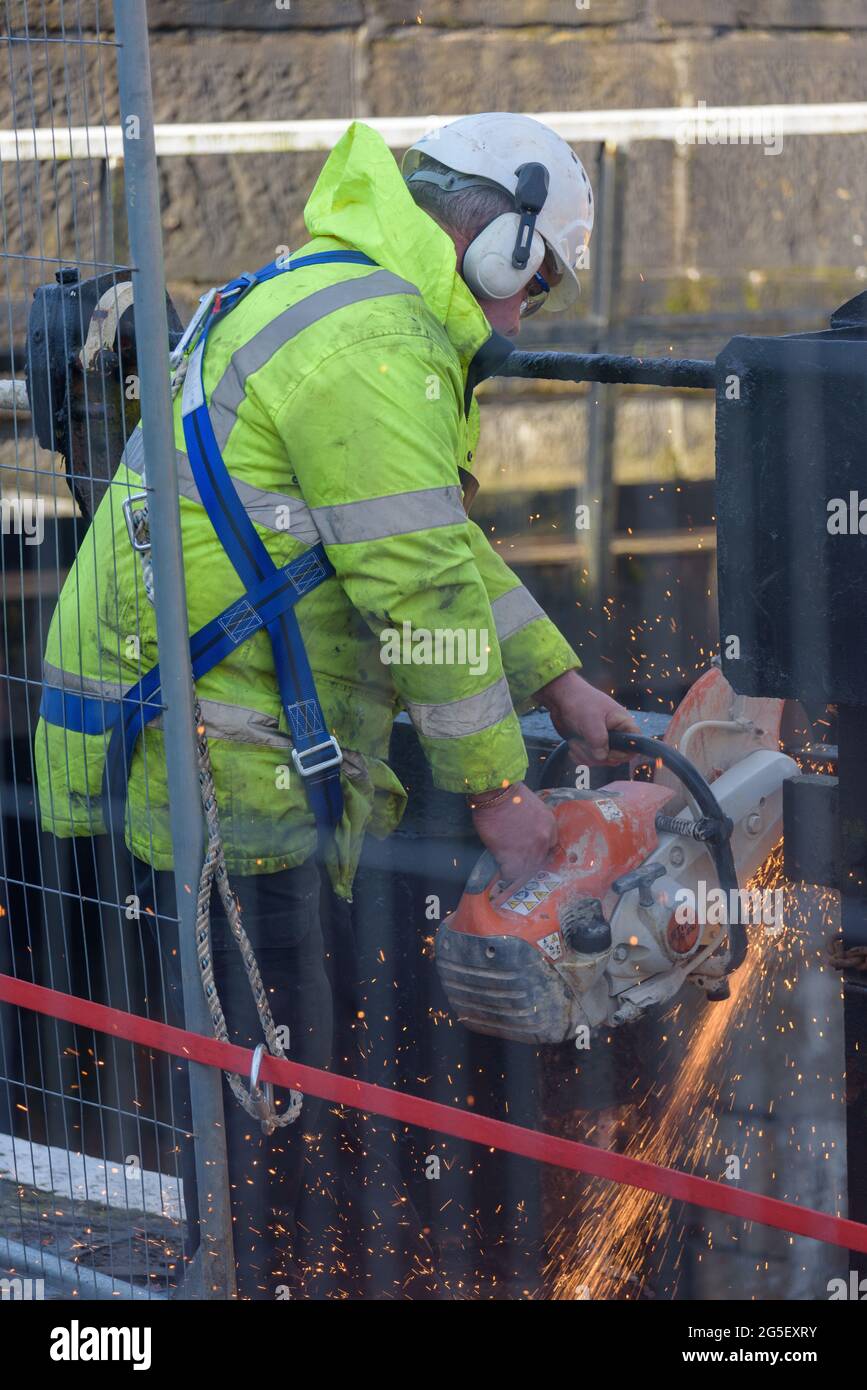 Un lavoratore maschile che utilizza una sega circolare per tagliare il metallo durante la sostituzione dei cancelli di blocco. Foto Stock