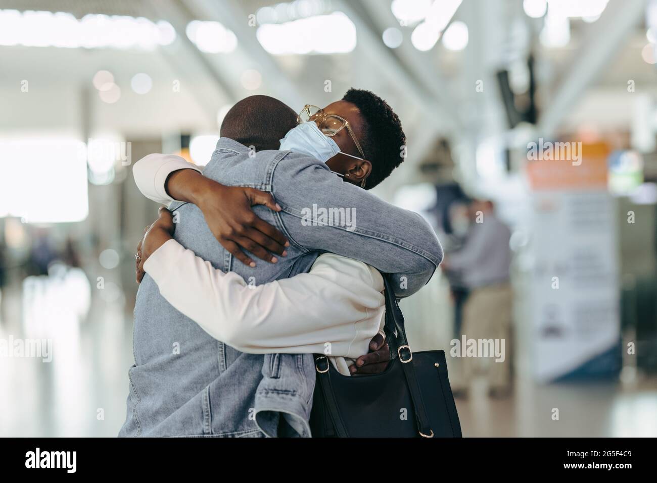Coppia di viaggiatori africani durante la riunione pandemica all'aeroporto. Uomo al terminal dell'aeroporto che abbraccia una donna con maschera facciale prima della partenza. Foto Stock