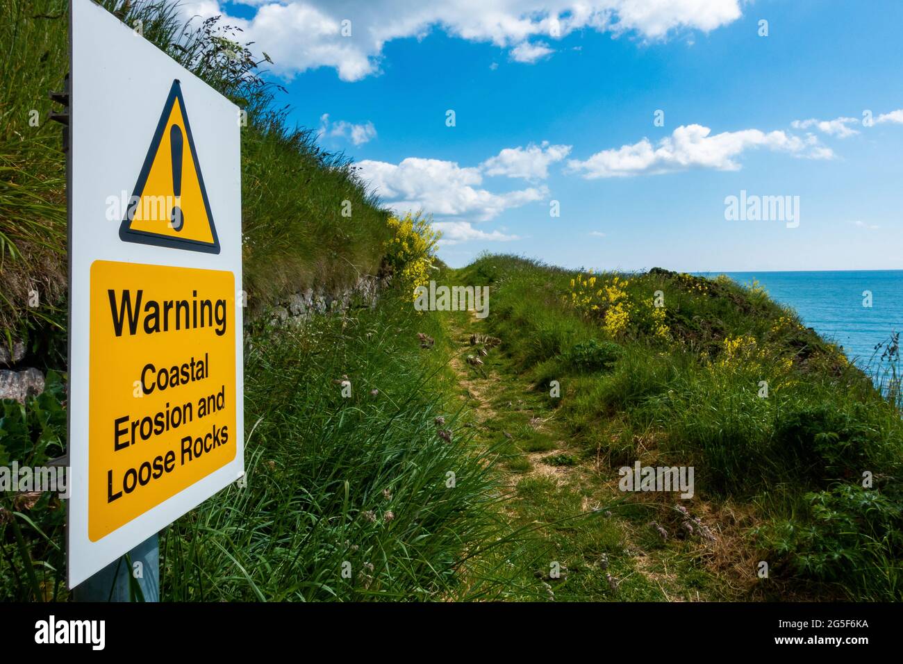 Un segnale di avvertimento circa erosione costiera e rocce sciolte su un percorso vicino Montrose, Scozia Foto Stock