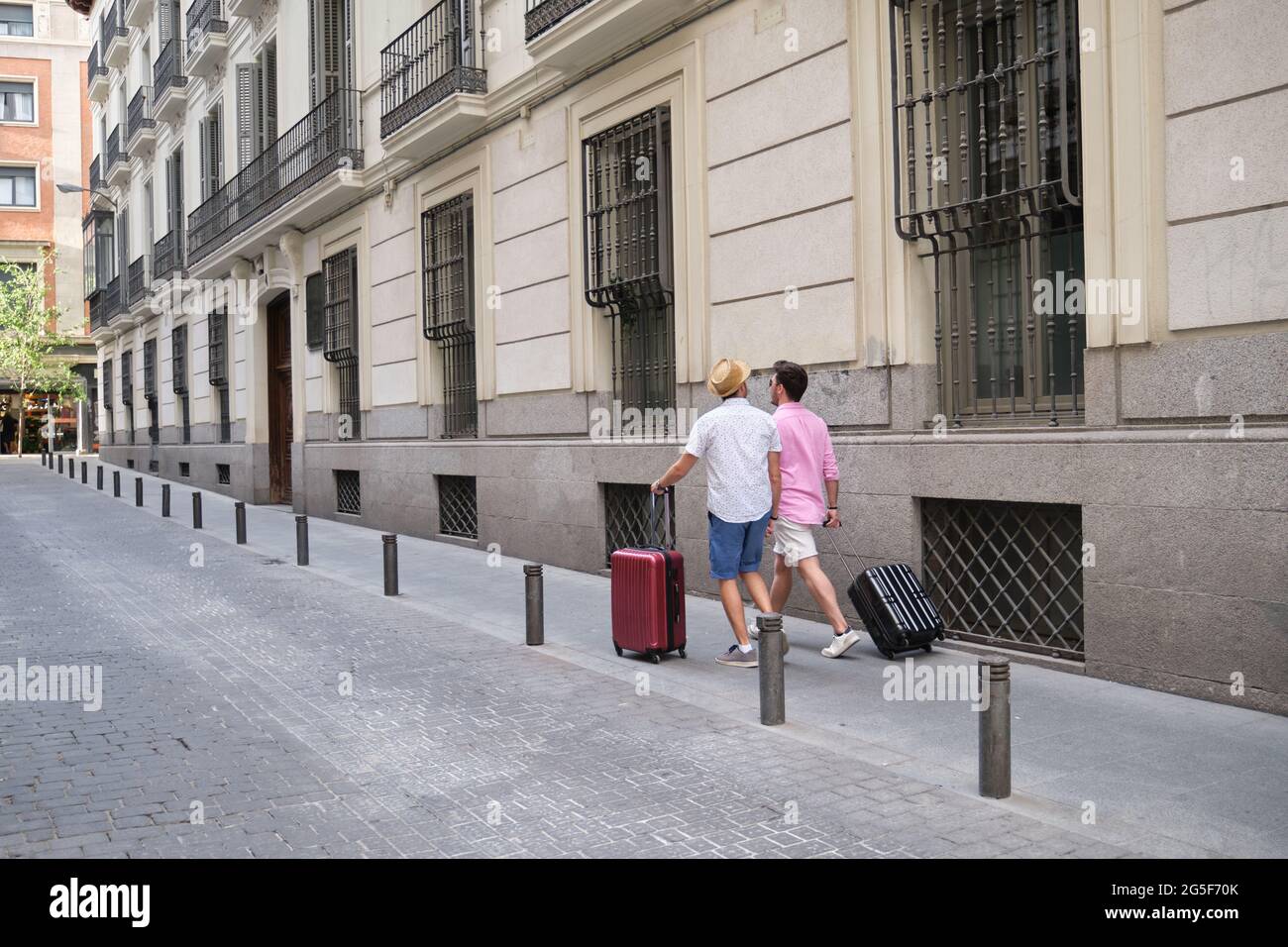 Due turisti che trasportano valigie e che vanno all'hotel in una strada cittadina. Foto Stock