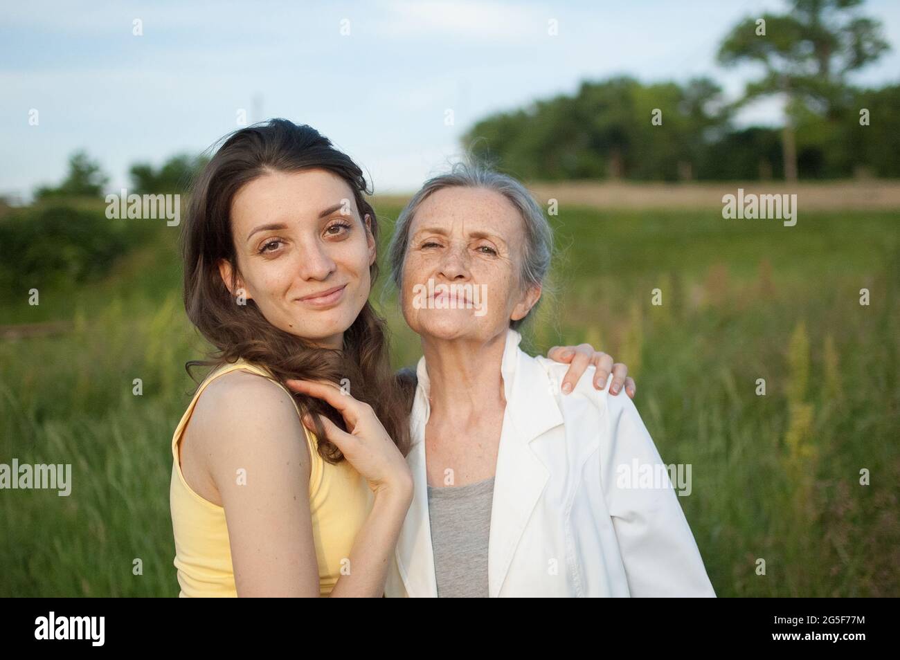 Madre anziana con i capelli grigi con la figlia adulta che guarda alla macchina fotografica nel giardino e abbracciandosi l'un l'altro durante una giornata di sole all'aperto Foto Stock