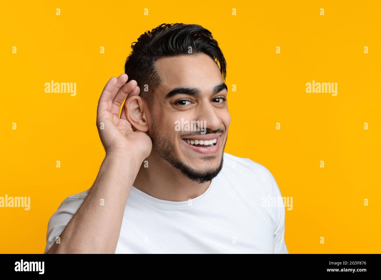 Ritratto closeup di un ragazzo arabo con un bell'orso che si sta abbellendo e sorridendo sullo sfondo giallo dello studio, bel giovane medio-orientale che tiene la mano Foto Stock