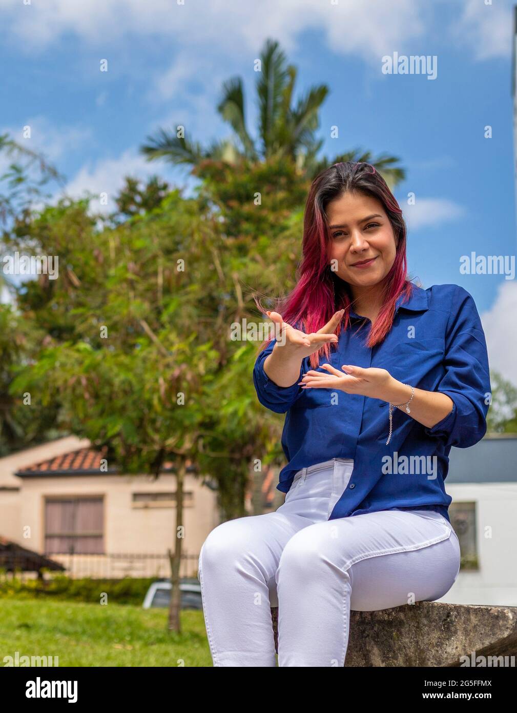 giovane donna seduta all'aperto facendo un gesto di benvenuto con le mani. Foto Stock