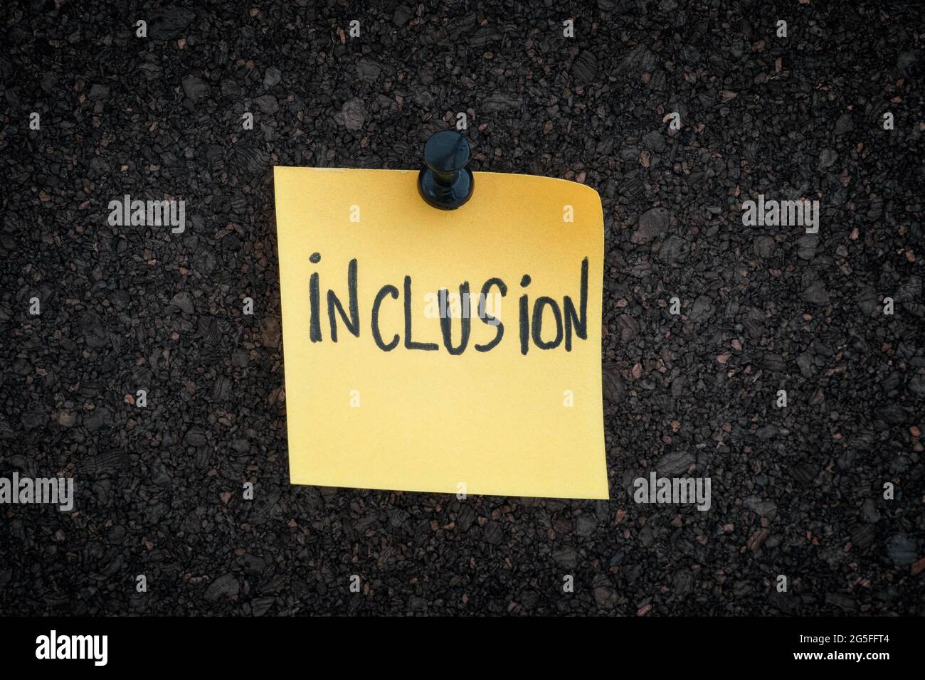 Inclusione. La parola inclusione scritta su una nota di carta gialla fissata su un pannello di sughero. Primo piano. Foto Stock