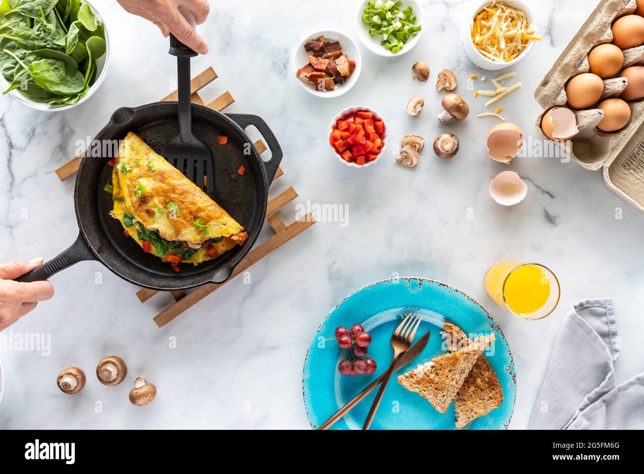 Vista dall'alto delle mani con una spatola che serve una frittata appena preparata, oltre agli ingredienti utilizzati per la preparazione. Foto Stock