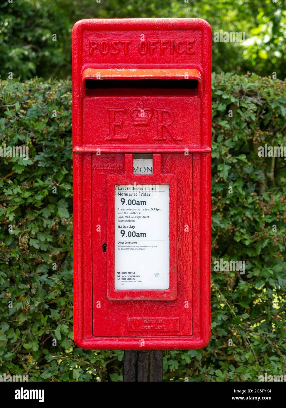 Scatola di lettere dell'ufficio postale in ghisa rossa montata su un montante di fronte a una siepe Foto Stock