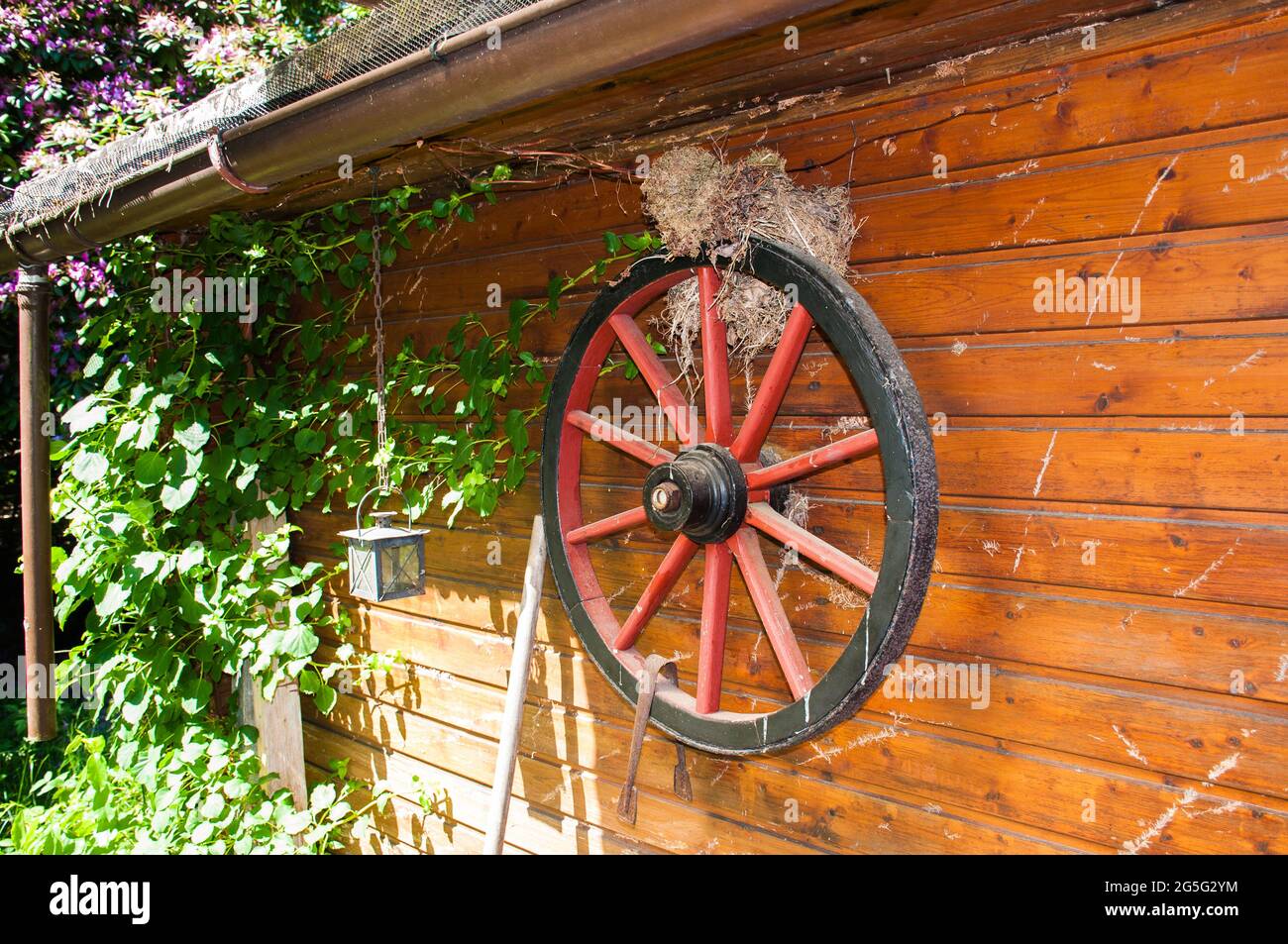 Decorazione su un capannone da giardino. Una vecchia ruota del carrello su cui un uccello ha costruito il suo nido Foto Stock