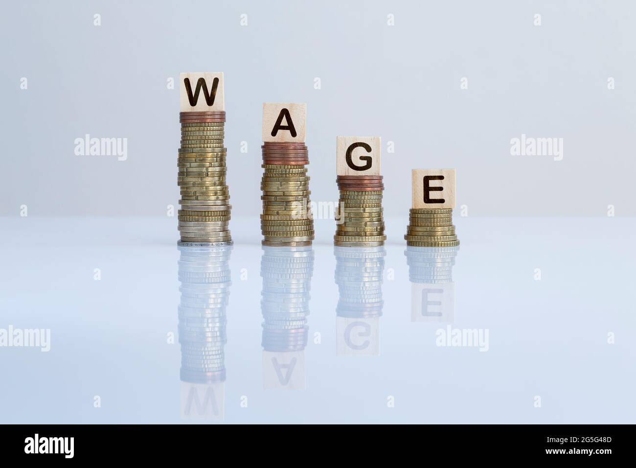 Parola 'SALARIO' su blocchi di legno in cima a pile discendenti di monete. Concept foto di perdita di denaro, crisi economica, recessione e riduzione finanziaria. Foto Stock