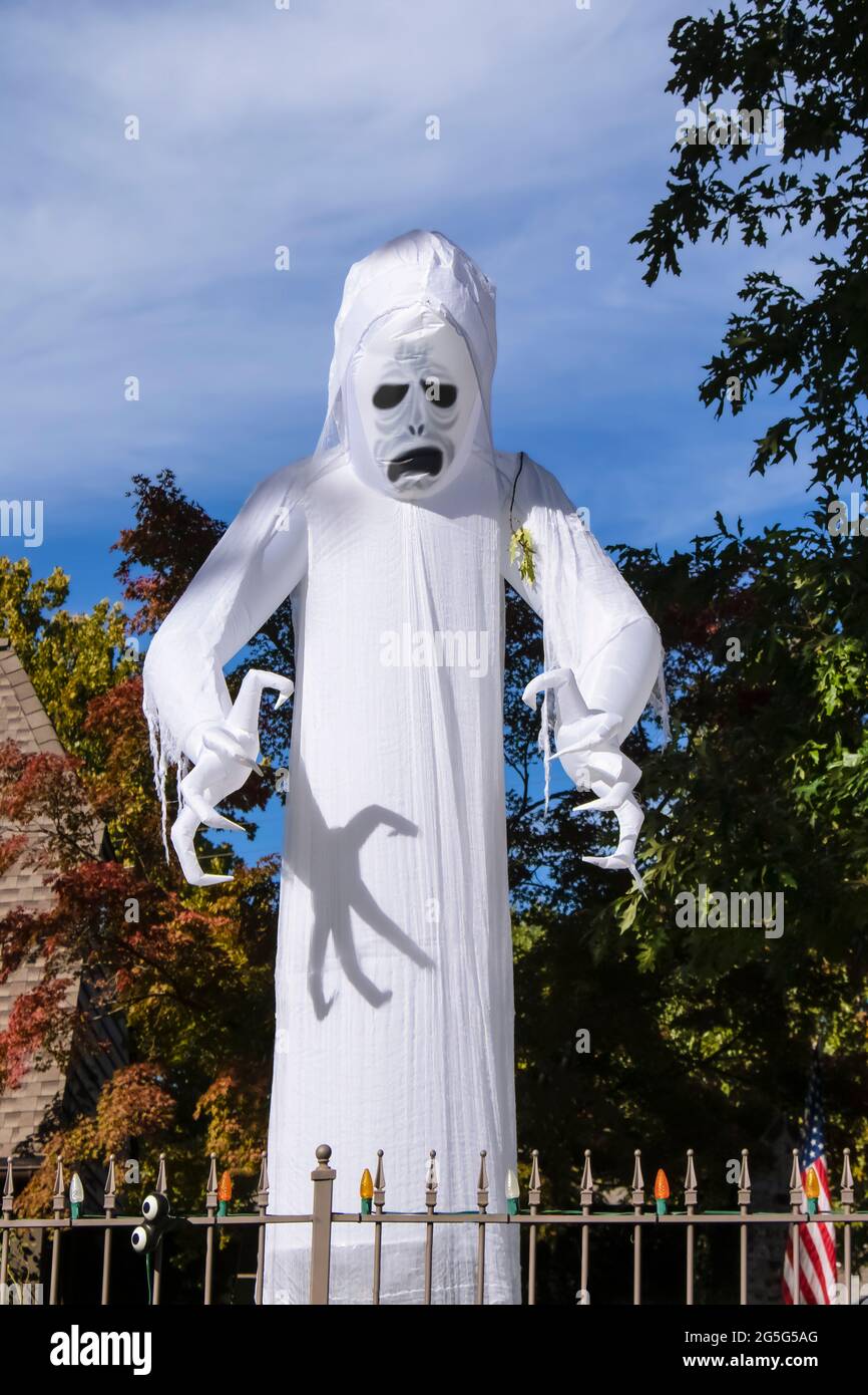 Spaventoso fantasma bianco gigante - zombie blowup Halloween decorazione torri sopra casa circondata da alberi autunnali con artigli pronti ad attaccare dietro recinzione WIT Foto Stock
