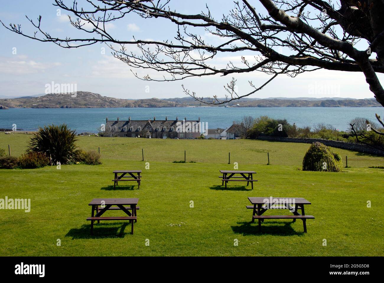 Quattro tavoli da picnic non occupati allestiti in una piacevole area verde che si affaccia sul mare, Iona, Scozia Foto Stock