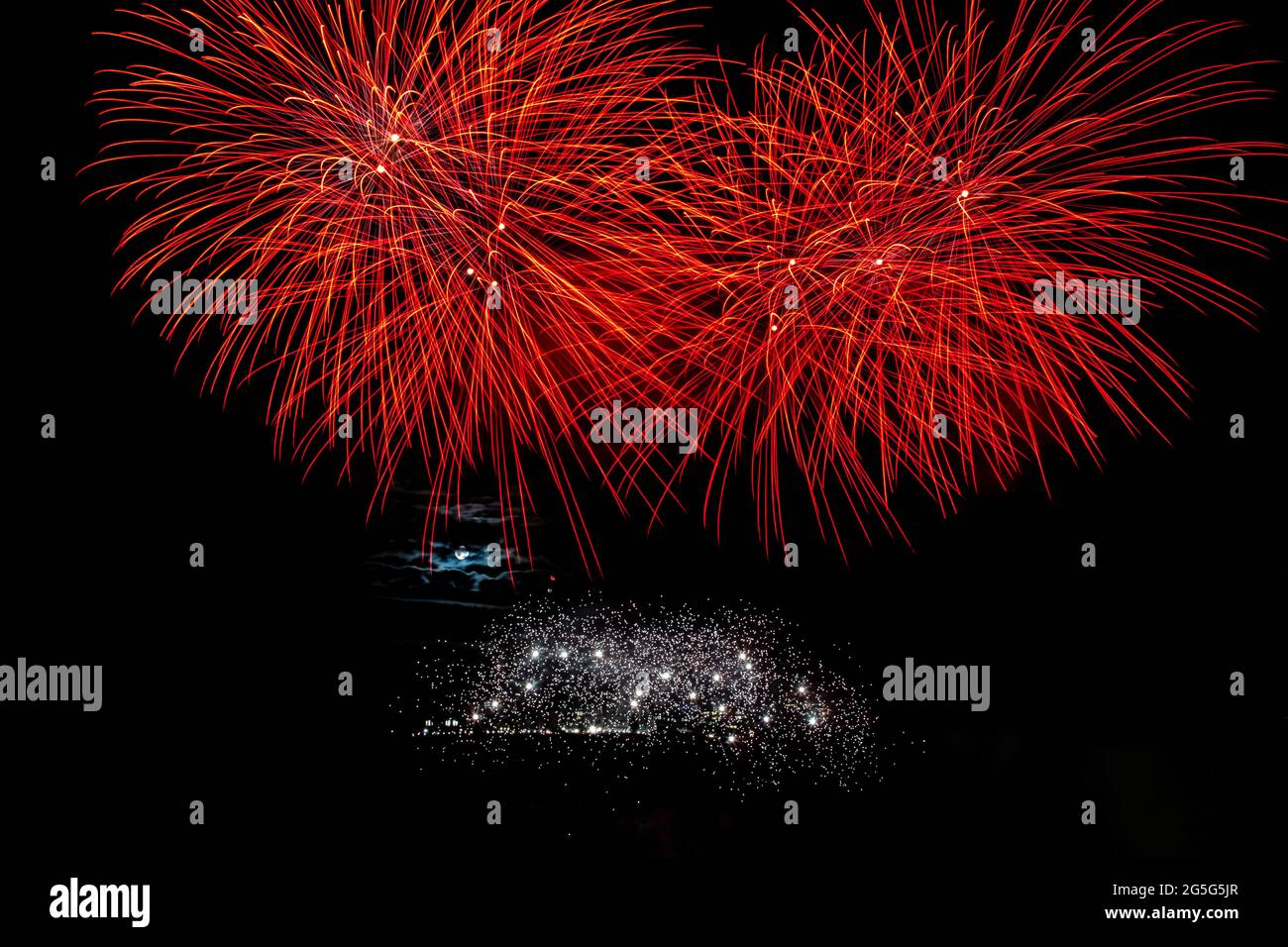 Esplosioni di fuochi d'artificio, sparklers bianchi e una luna piena parzialmente coperta dalla luna Foto Stock