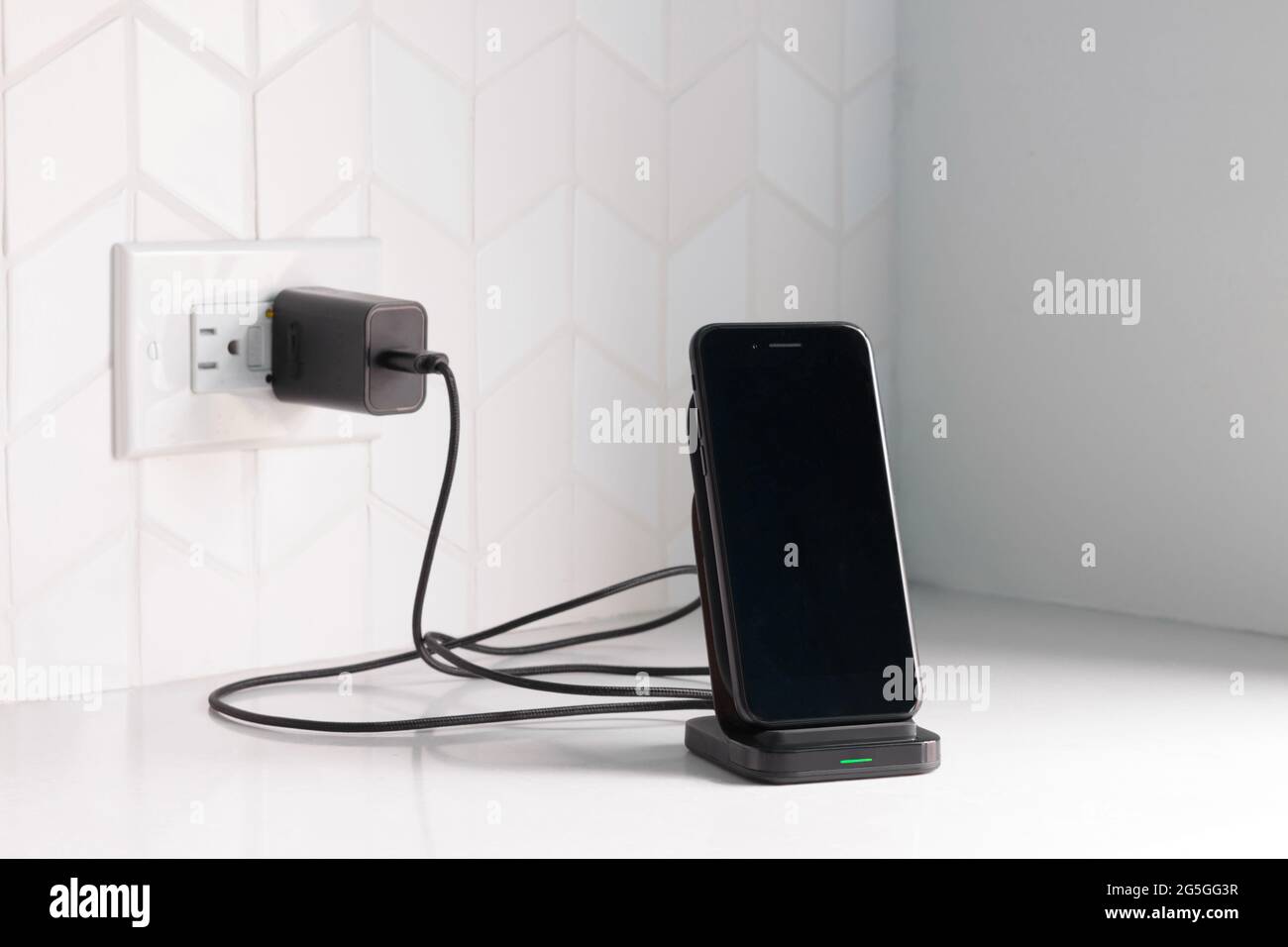 uno smartphone nero inserito in una stazione di ricarica wireless collegato a un banco da cucina bianco o a un banco con spazio per la copia Foto Stock