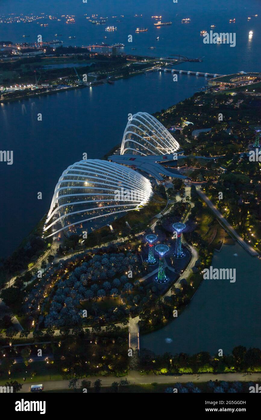 Vista dei Giardini di Singapore presso la Baia mentre il sole tramonta e le luci si accendono, con molte navi nel trafficato stretto di Singapore oltre Foto Stock