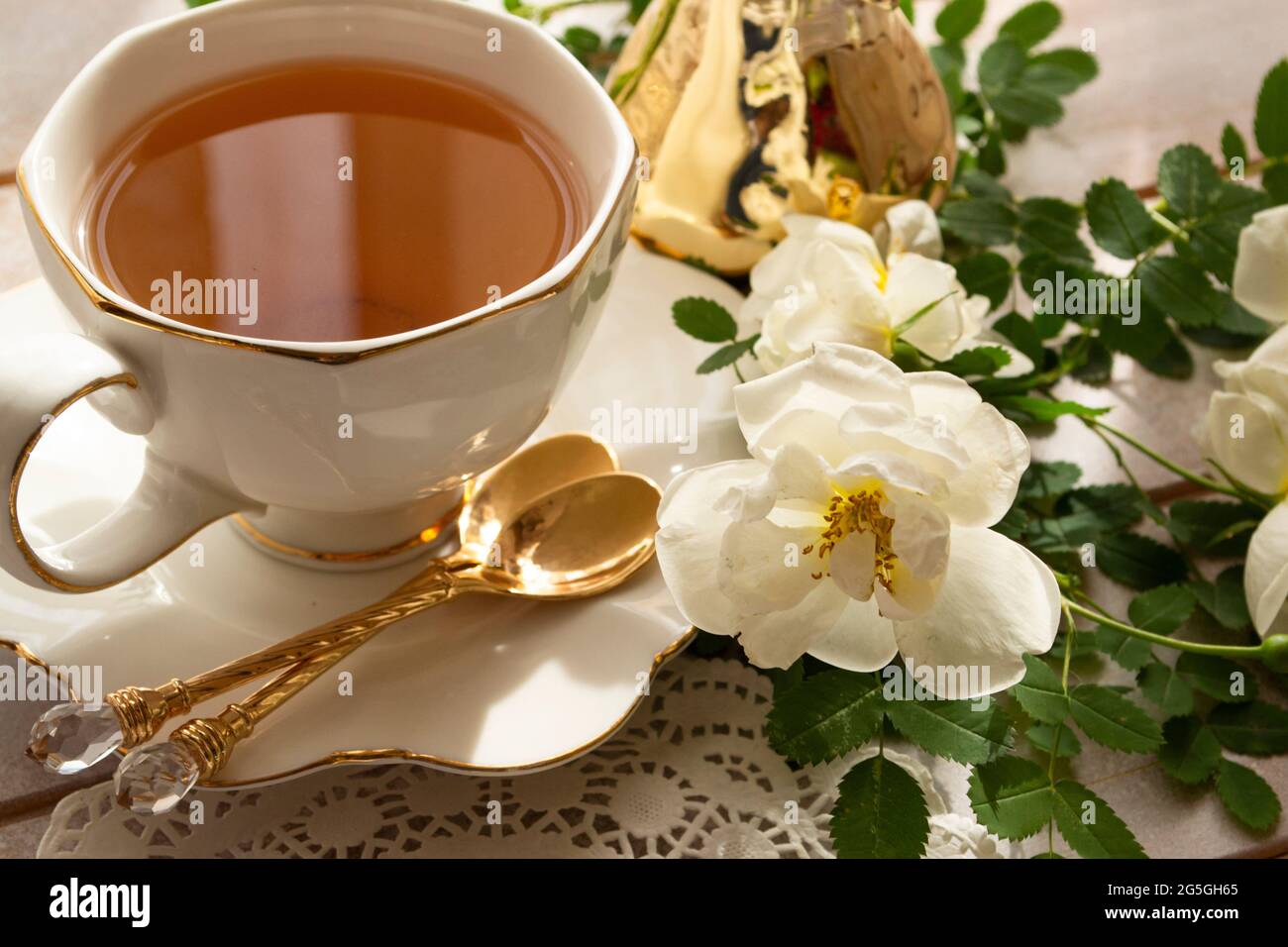 Tazza di tè e rametto di piccole rose bianche su tavola rustica, in colori bianco e oro Foto Stock