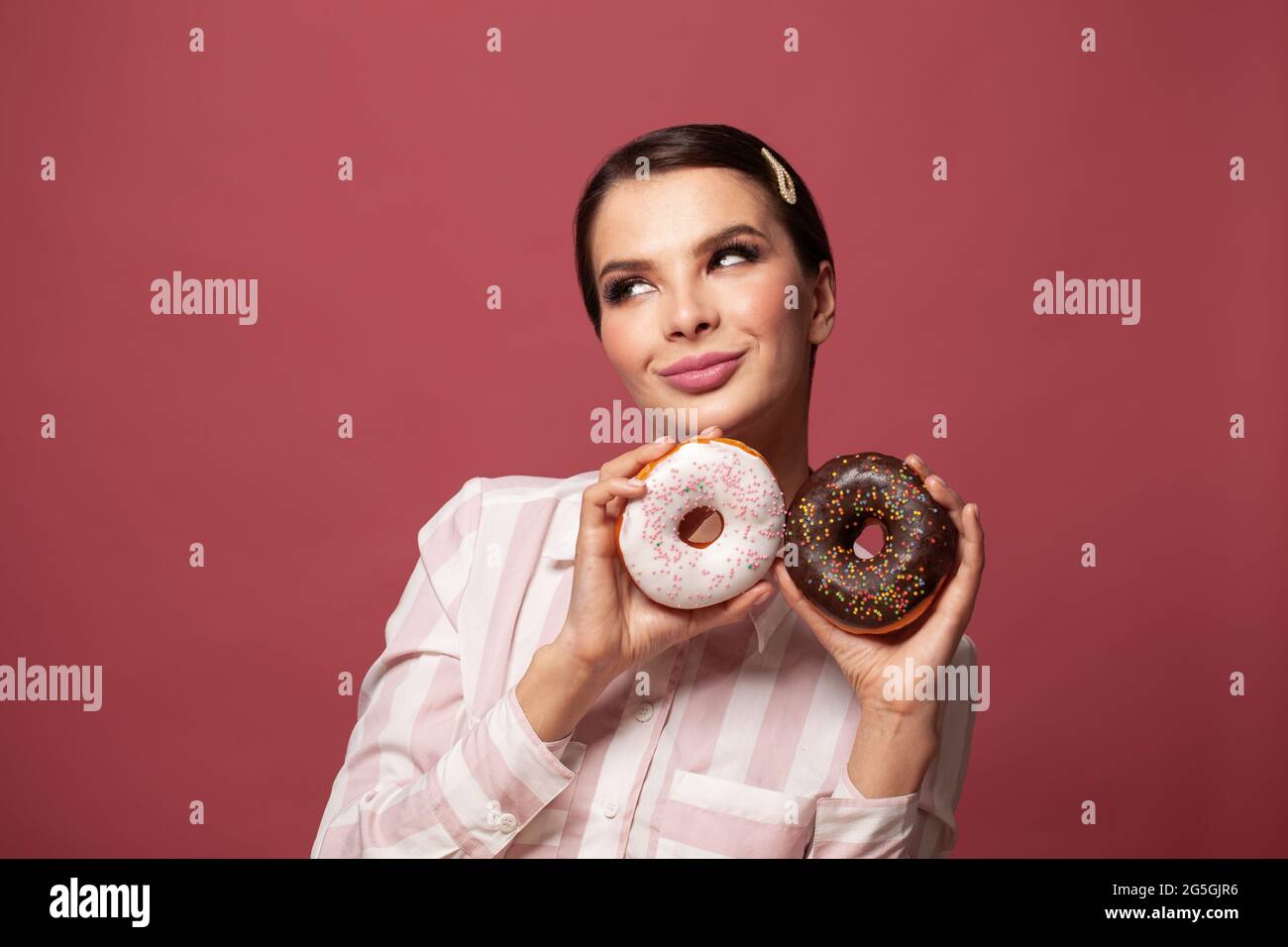 Donna bruna sorridente con ciambella di zucchero e cioccolato e guardando su sfondo rosso Foto Stock