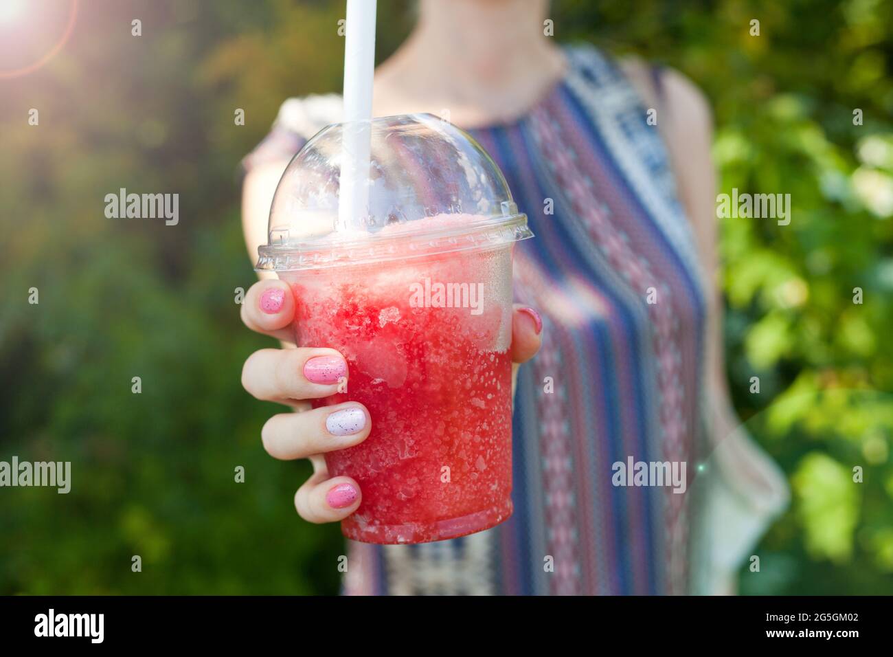 Mano donna che tiene acqua di ghiaccio rosso in tazza di plastica. Bevanda ghiacciata - bevanda estiva fredda e sana o cocktail. Giornata di sole Foto Stock