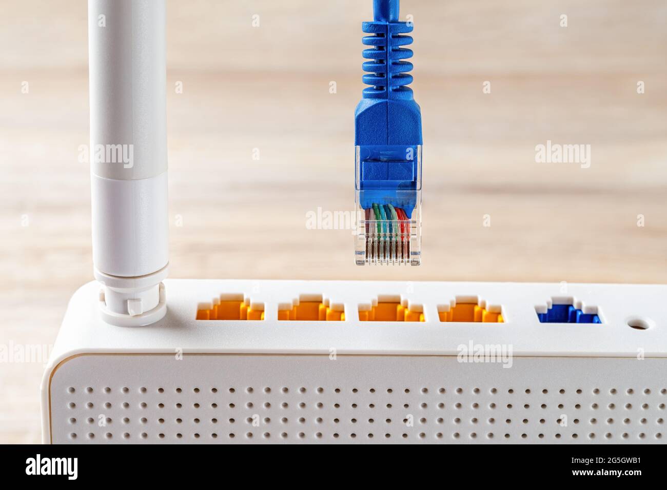 La macro della spina blu del cavo di rete è quasi inserita nella presa gialla del router wireless wi-fi bianco. Router WLAN per Internet a casa e in ufficio. Foto Stock