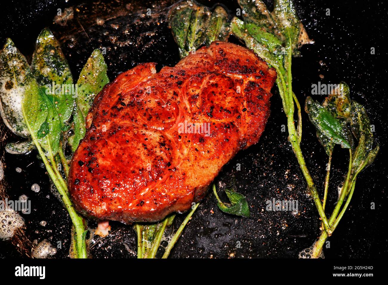 costolette di maiale marinate alle erbe, cottura a vista con salvia con una griglia calda Foto Stock
