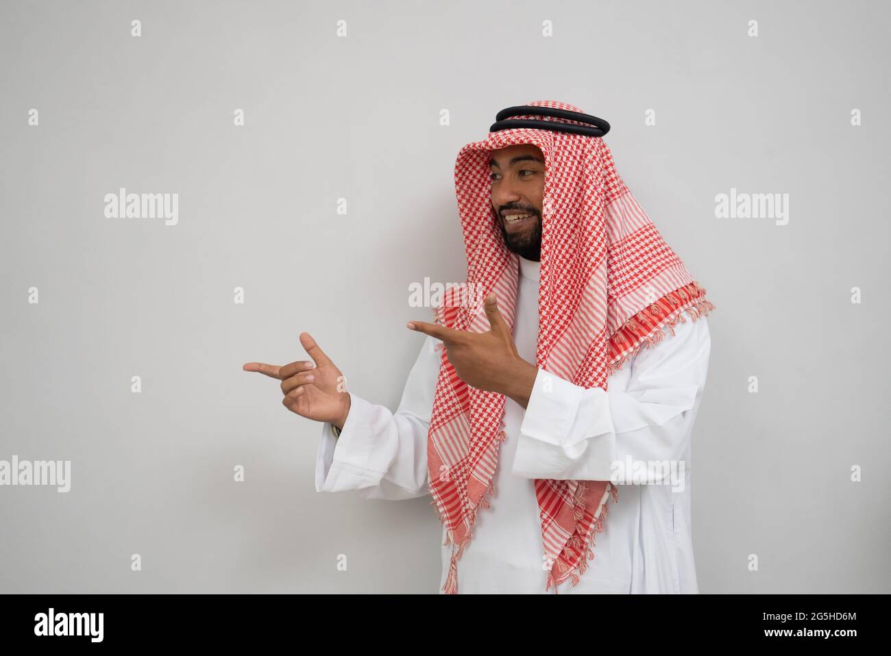 un giovane arabo in un turbante sorridente mentre si sta in piedi con un gesto della mano che indica di presentare qualcosa Foto Stock