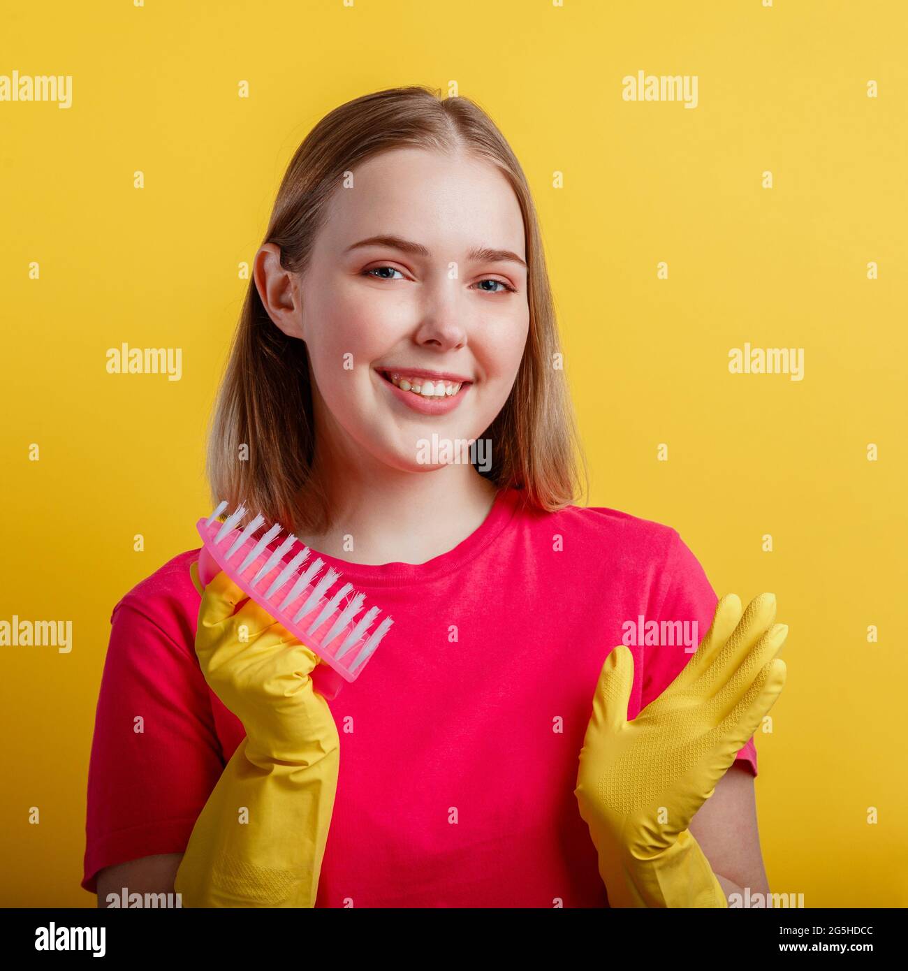 Donna Ritratto con spazzola di pulizia in guanti di gomma. Giovane bionda felice donna sorridente pronta a pulire casa con forniture per la casa isolato sopra Foto Stock