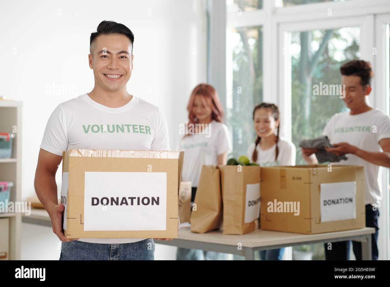 Ritratto di felice giovane che lavora in fondazione caritatevole e imballaggio di scatole di donazione per banca alimentare Foto Stock