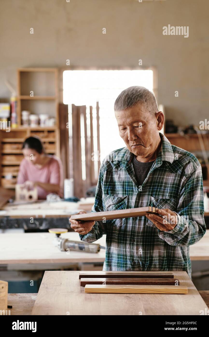 Carpentiere concentrato che controlla la qualità dei pezzi di legno di noce e acero fusi insieme Foto Stock