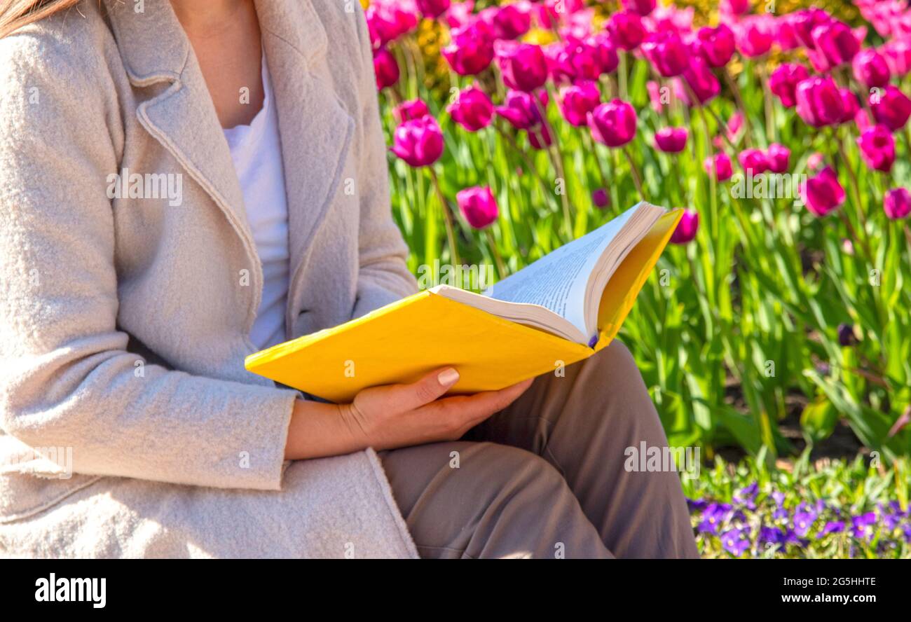 Una ragazza con un libro giallo si siede su uno sfondo di tulipani rosa. Messa a fuoco selettiva. Foto Stock