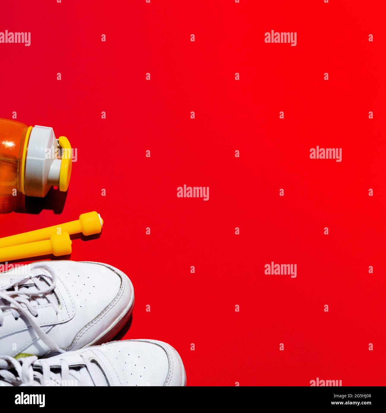 Sneaker bianche con corda gialla e bottiglia d'acqua. Sfondo rosso con spazio per il testo. Messa a fuoco selettiva. Foto Stock