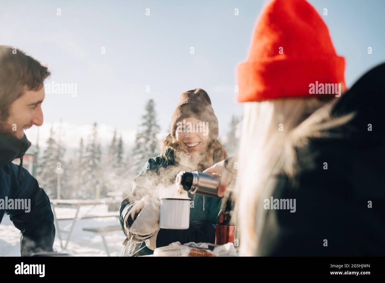 Giovane donna che versa il caffè per un'amica durante l'inverno Foto Stock