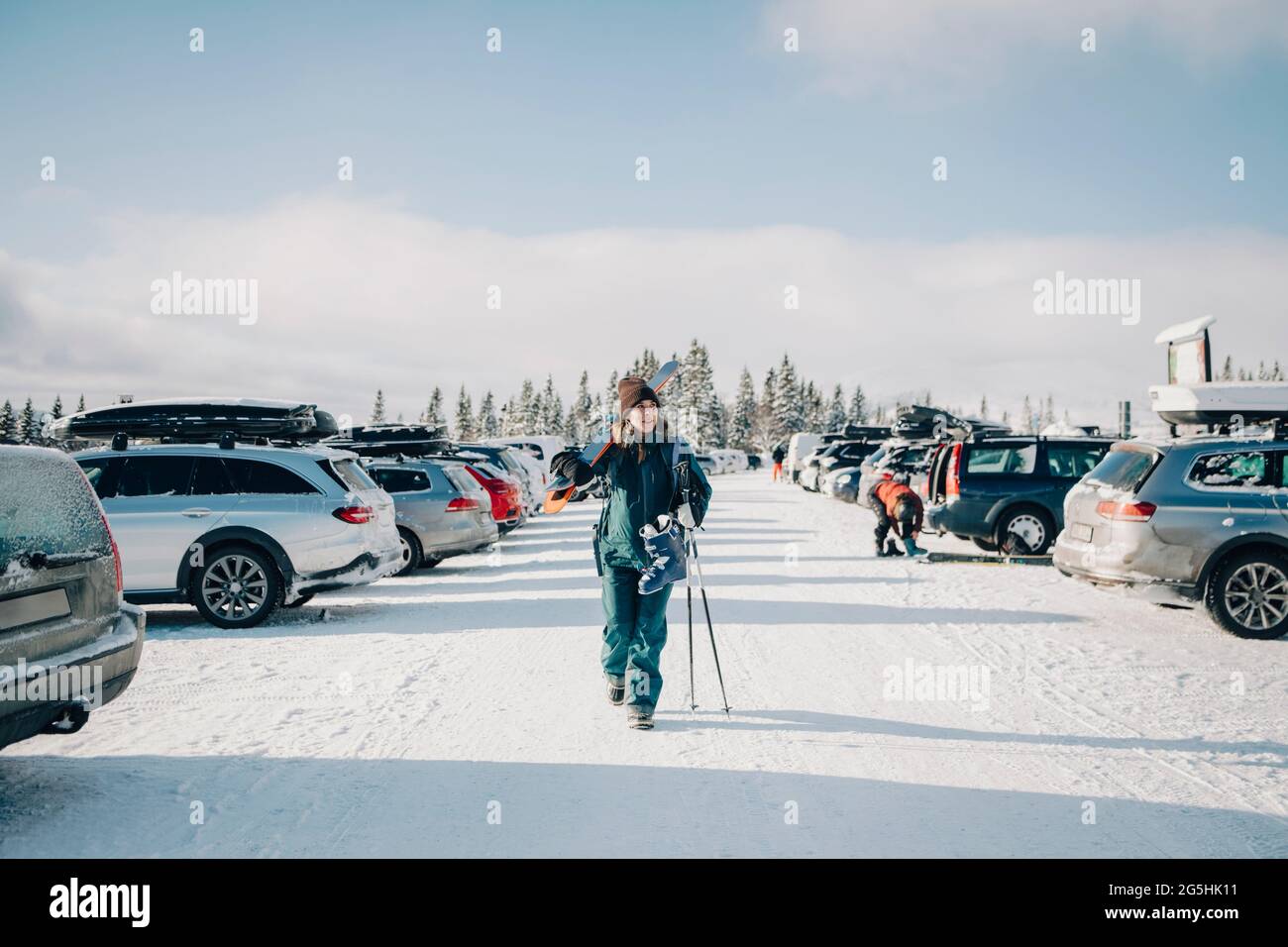 Una donna che guarda via mentre cammina tra le auto nel parcheggio contro il cielo Foto Stock