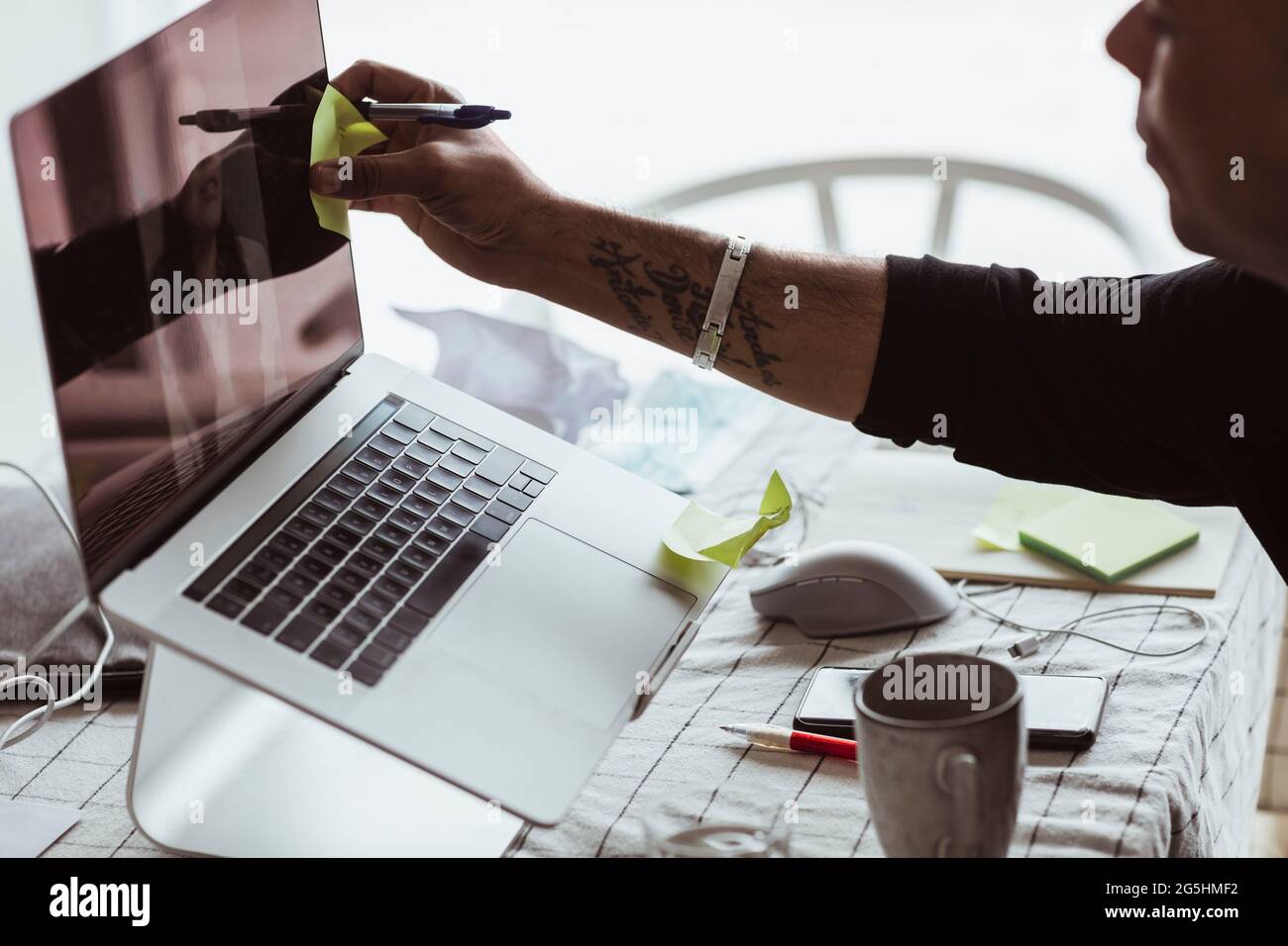 Immagine ritagliata di una nota adesiva appiccicata da un uomo d'affari sullo schermo del dispositivo durante la videoconferenza a casa Foto Stock