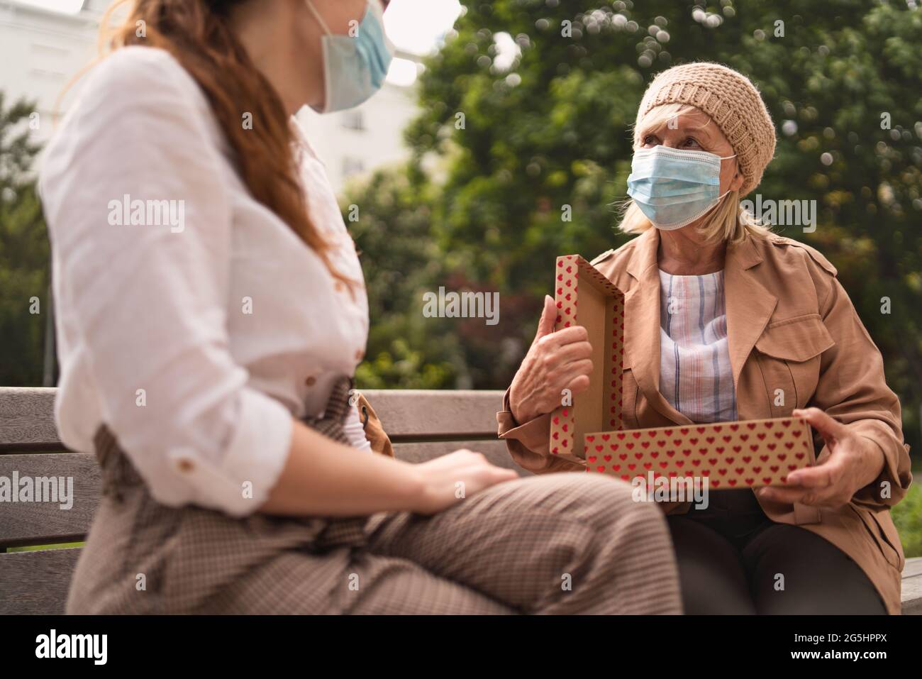 Giovane donna che dà presente a nonna all'aperto in città, la vita dopo la vaccinazione covid-19. Foto Stock