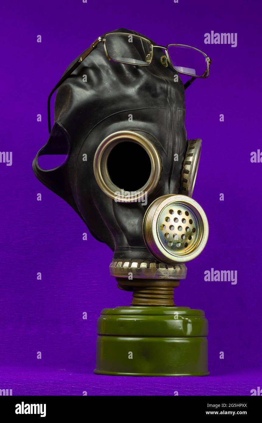 Una vecchia maschera a gas dell'esercito e occhiali da lettura su uno sfondo lilla. Protezione personale contro le armi chimiche e radiologiche, nonché contro le infezioni velenose Foto Stock