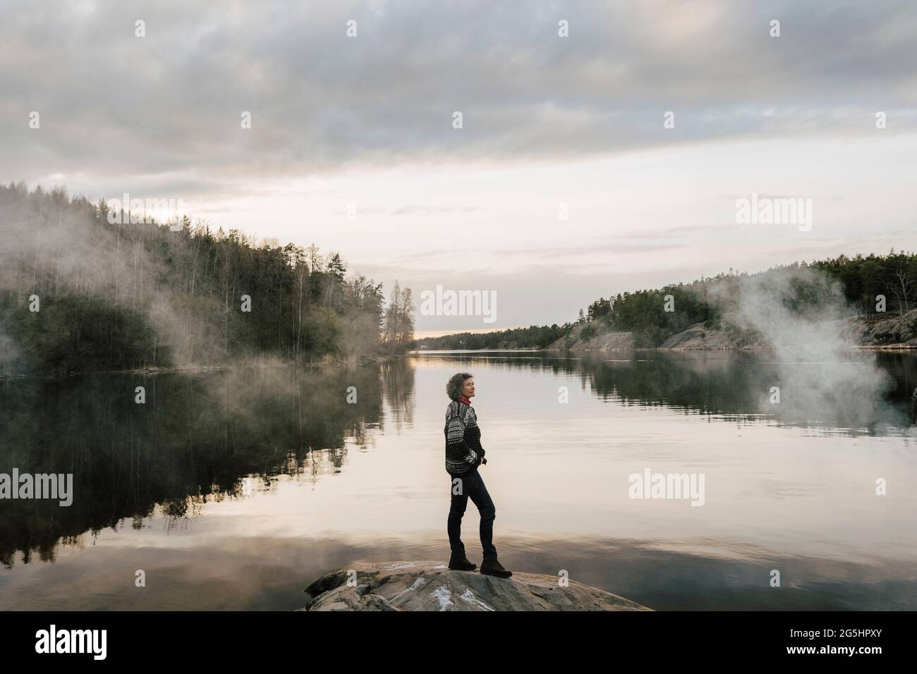esploratore femminile maturo in piedi sulla roccia vicino al lago Foto Stock
