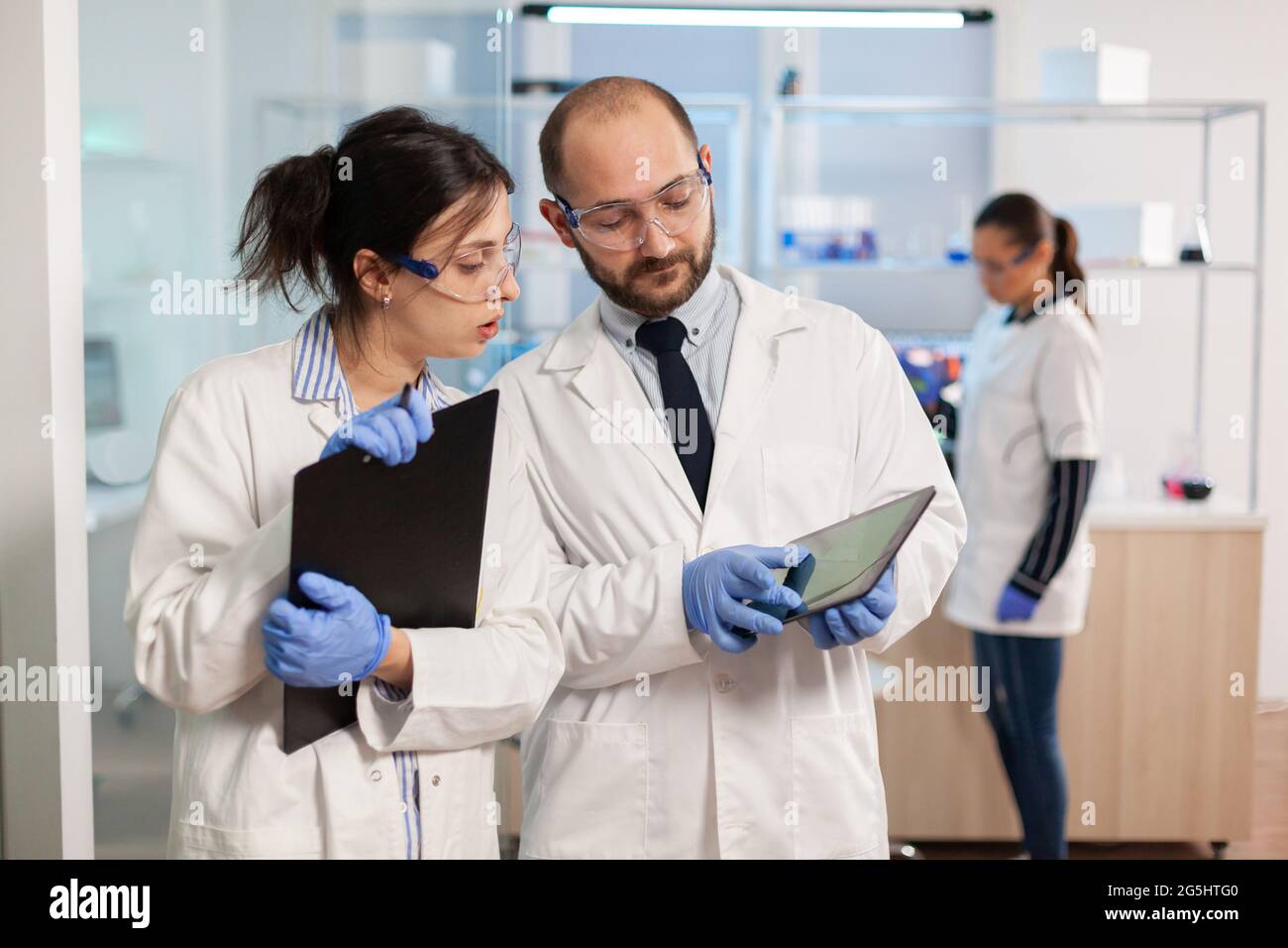 Gruppo di ricercatori medici che discutono sullo sviluppo di vaccini, in  piedi in laboratorio attrezzato puntando su tablet e prendendo appunti. I  medici che esaminano l'evoluzione del virus usando la diagnosi di