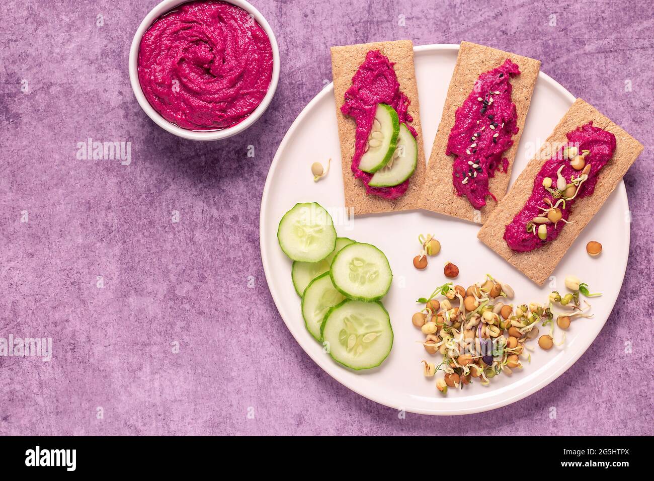 Spuntino vegetariano, vegano - hummus di barbabietola, grani germogliati, cetriolo e croccanti di grano intero. Foto Stock