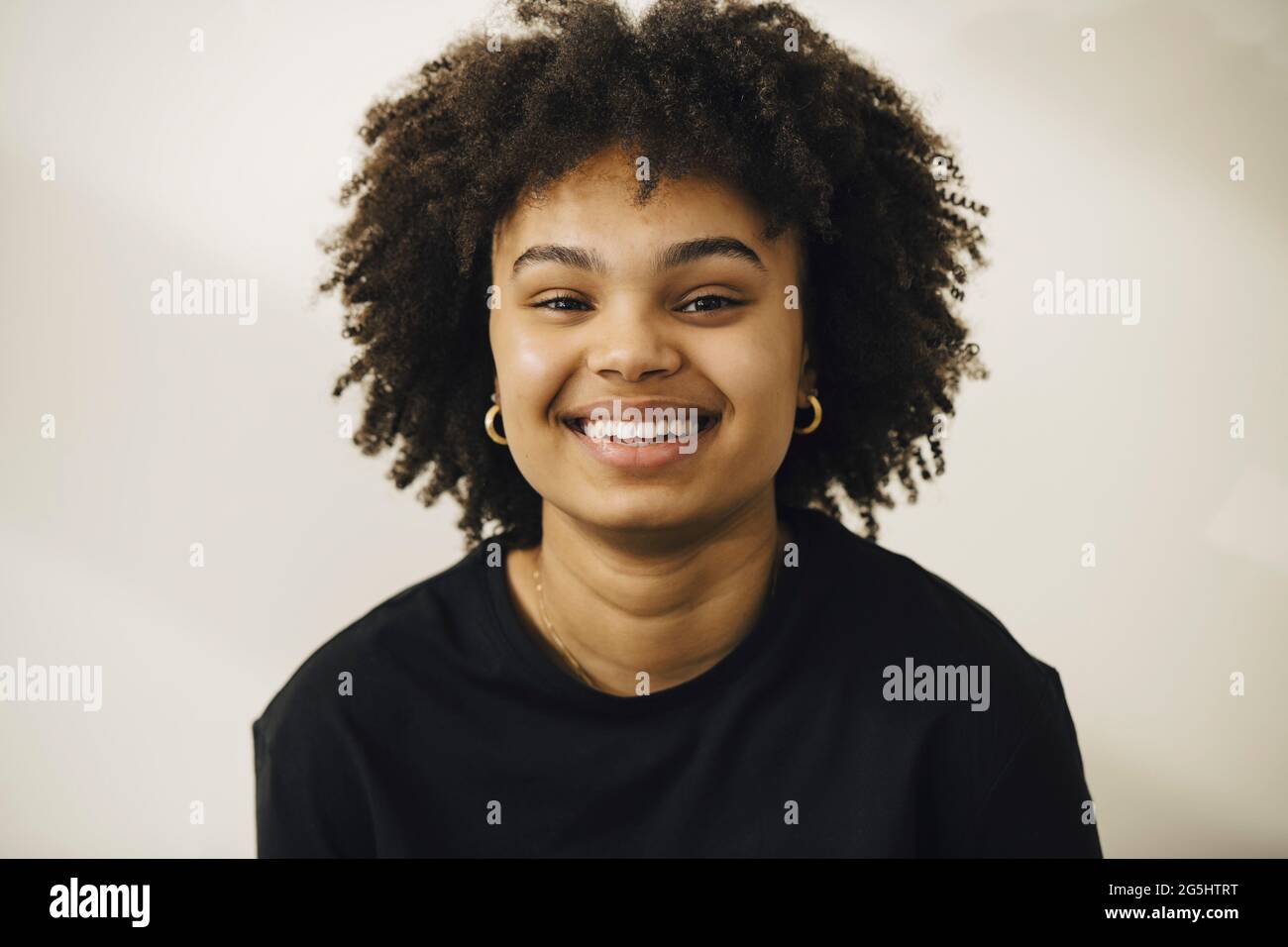 Giovane donna sorridente con capelli ricci su sfondo beige Foto Stock