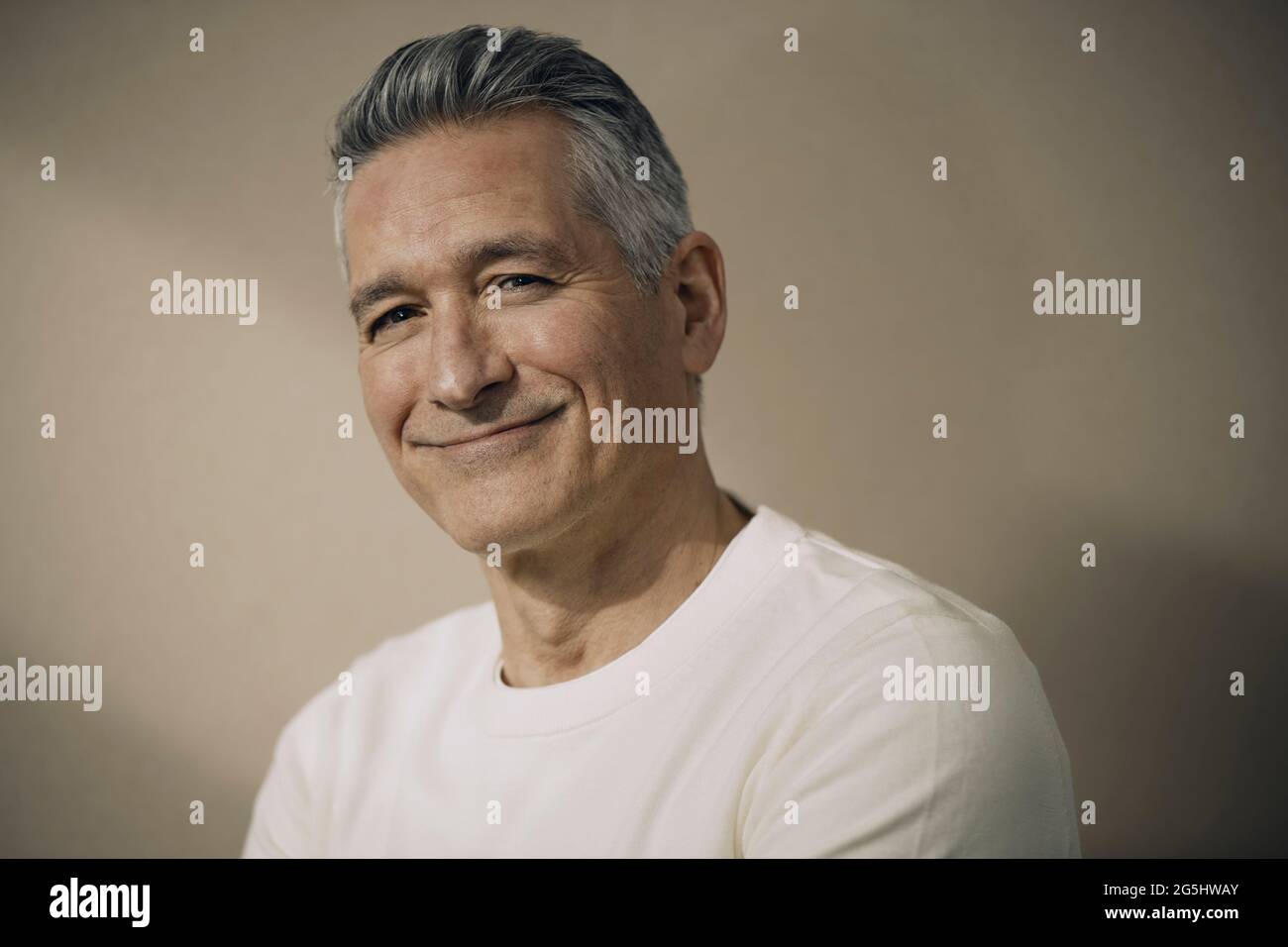 Uomo maturo sorridente con capelli grigi contro parete beige Foto Stock