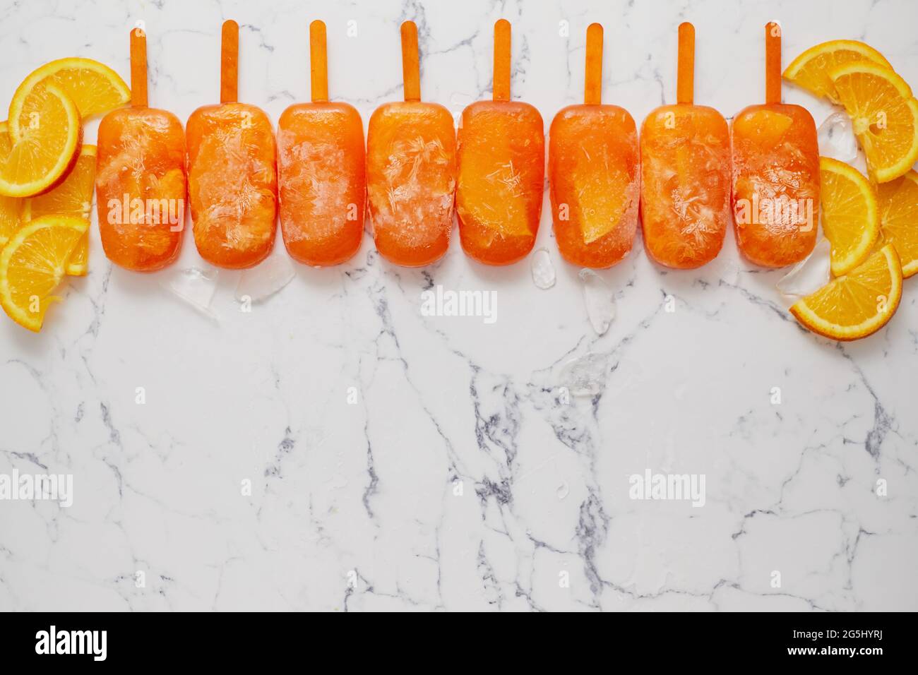 Pop sicle surgelate fatte in casa con arance fresche oragniche poste con cubetti di ghiaccio sul tavolo di marmo Foto Stock