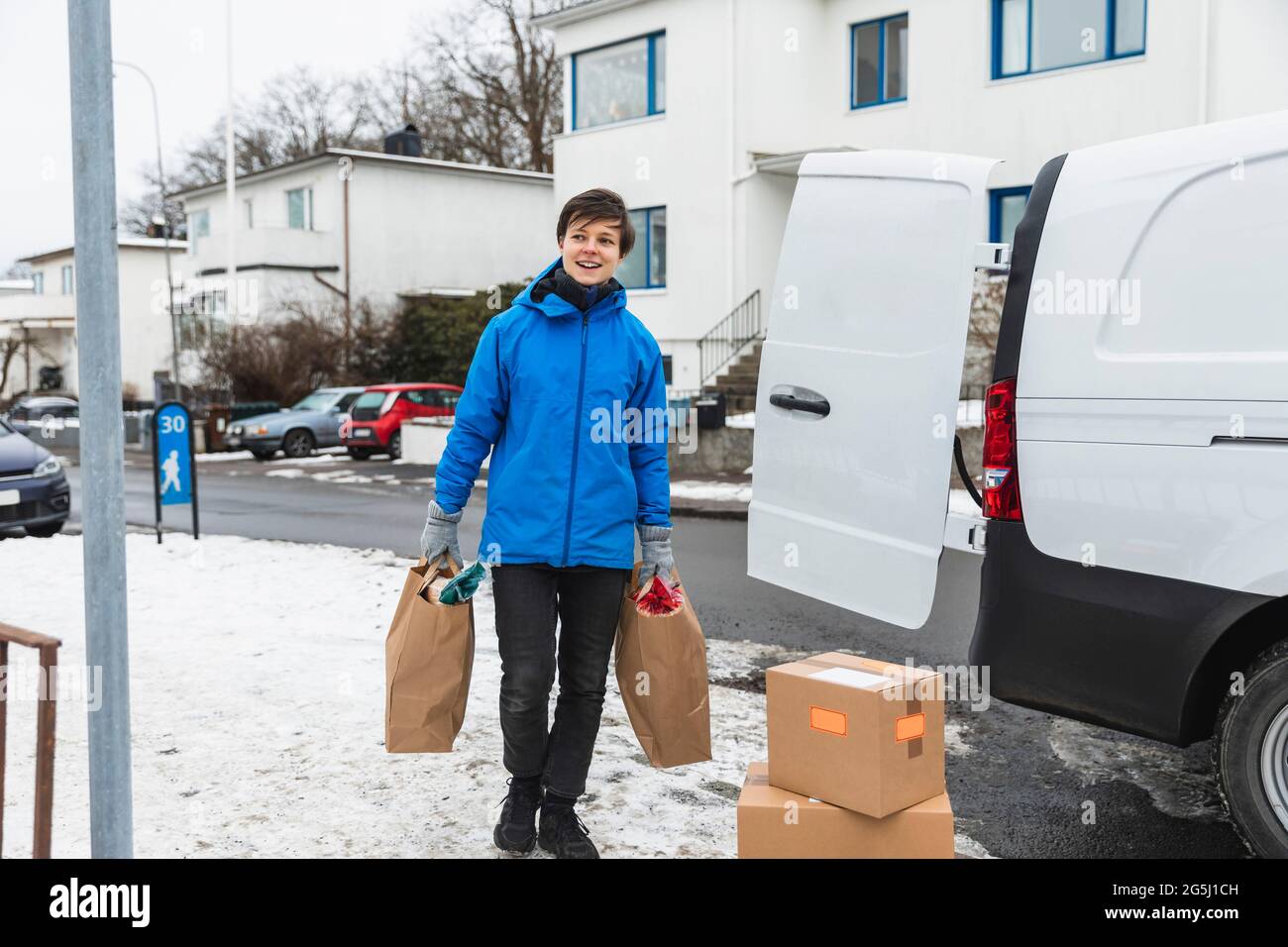 Sorridente donna di servizio essenziale che consegna sacchetti di carta durante l'inverno Foto Stock